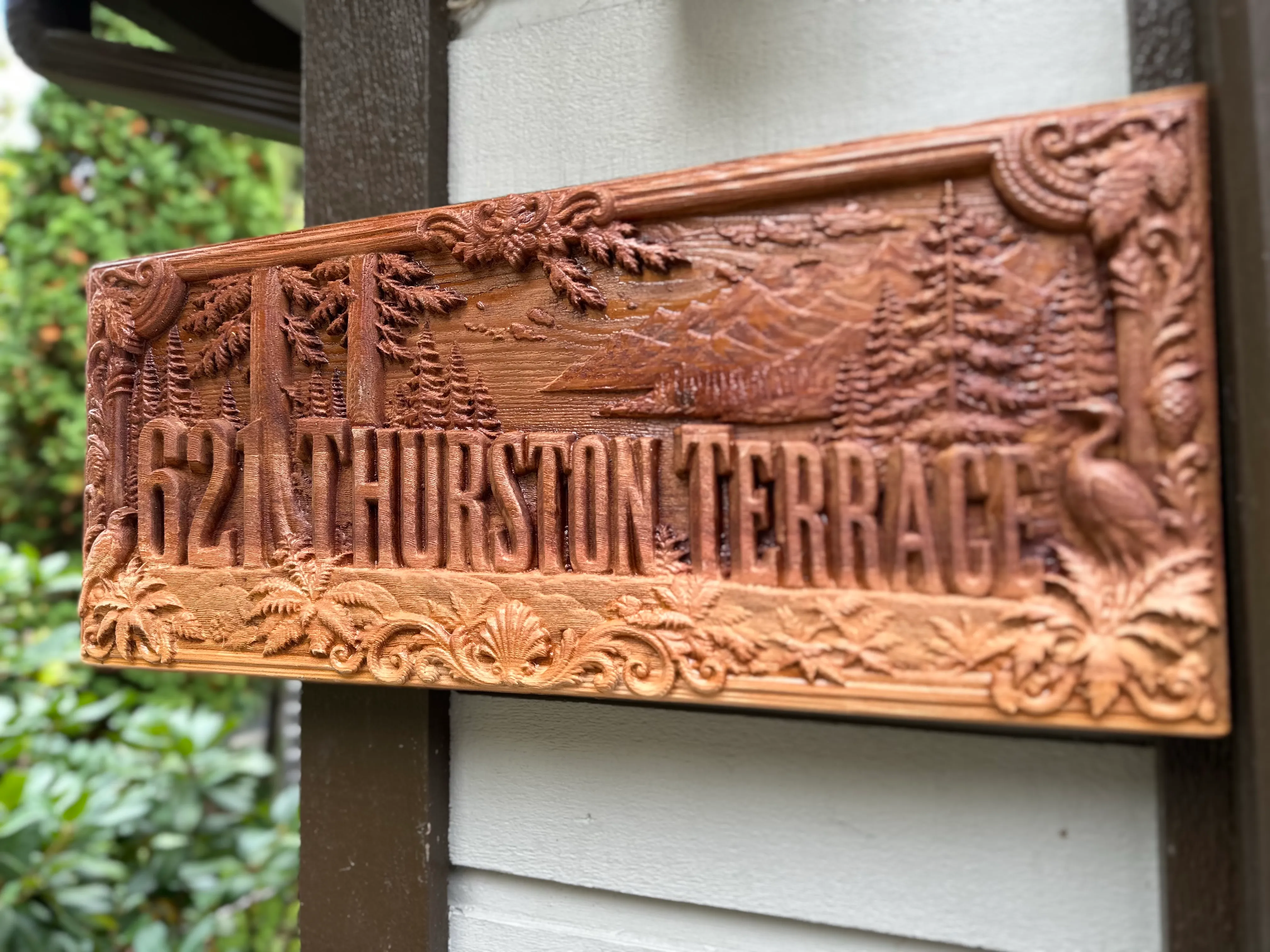 Pacific Northwest style: 621 Thurston Terrace sign with cedars, mountains, ferns and a heron, mounted on a house